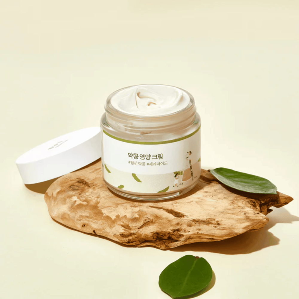 Mixsoon Soybean Nourishing Cream v odprti posodi na leseni površini z zelenimi listi. Hranilna krema s fermentiranimi sojinimi zrni in ceramidi.