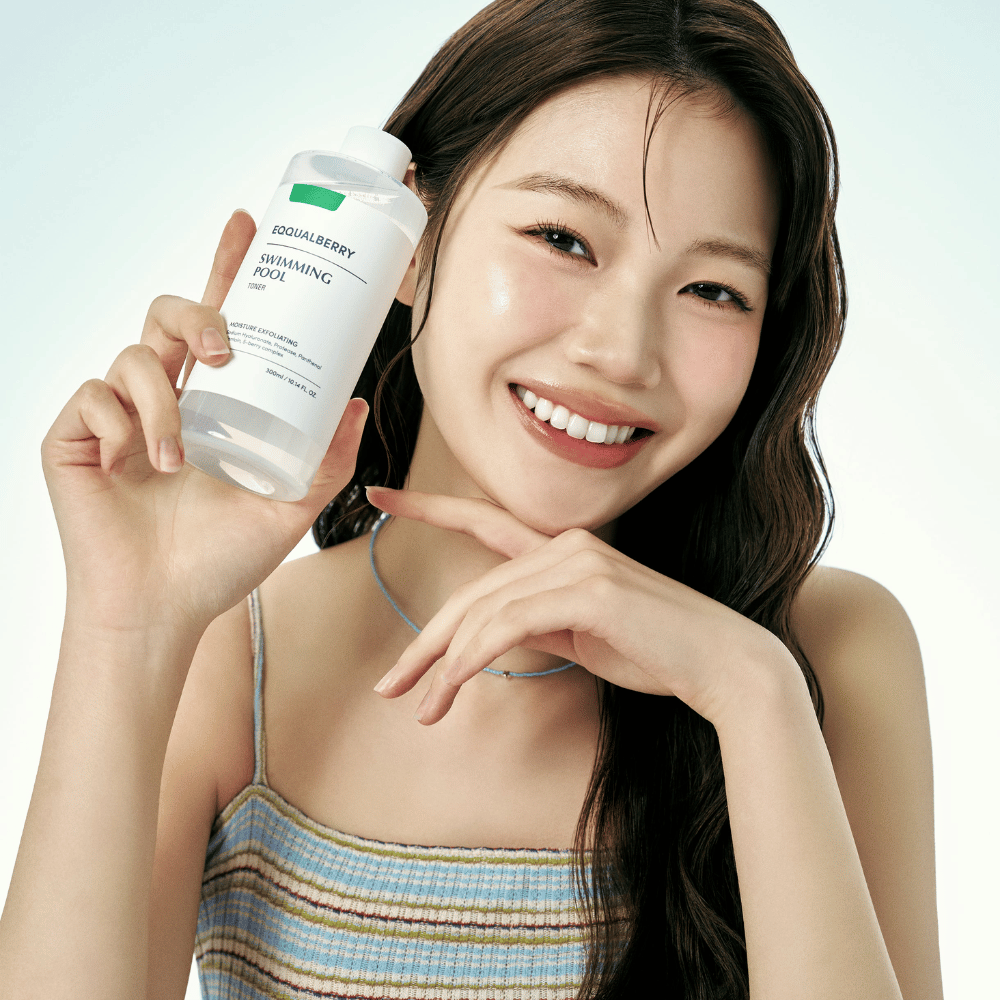 Nasmejana ženska s sijočo kožo drži Equalberry Swimming Pool Toner. Svež in naraven videz z lahkim ličenjem in poletno obleko v modrih tonih.