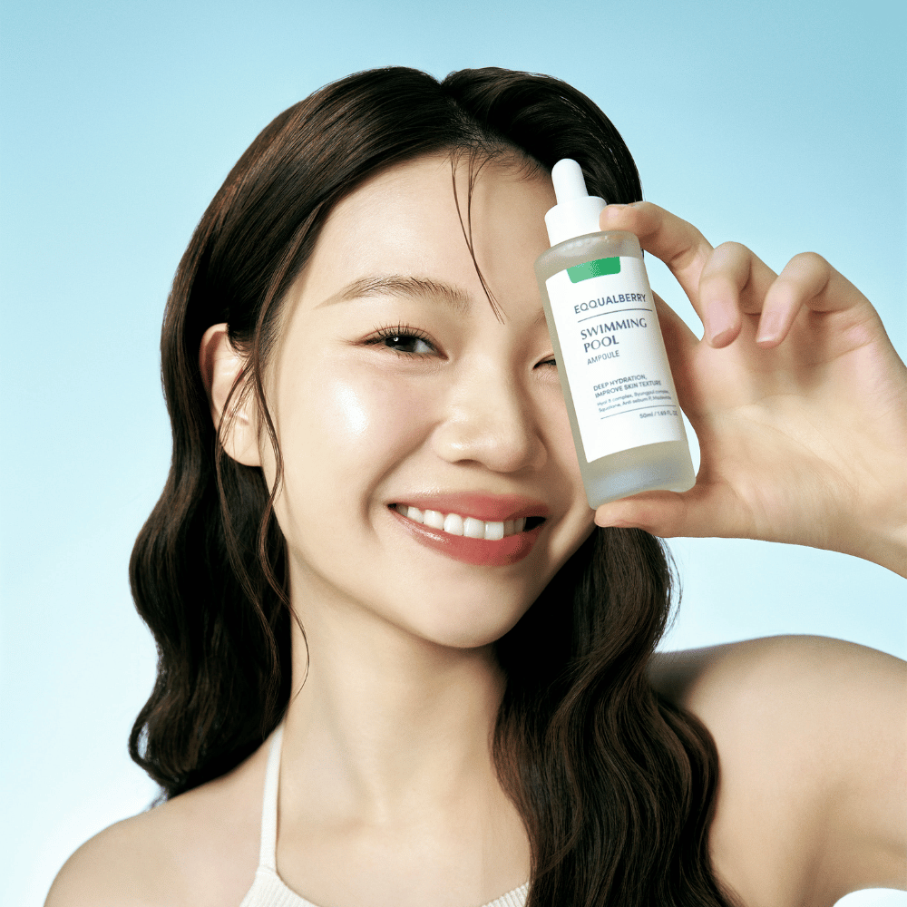 Nasmejana ženska drži Eqqualberry Swimming Pool Ampoule, izdelek za nego kože za intenzivno vlaženje, na svetlo modri podlagi.