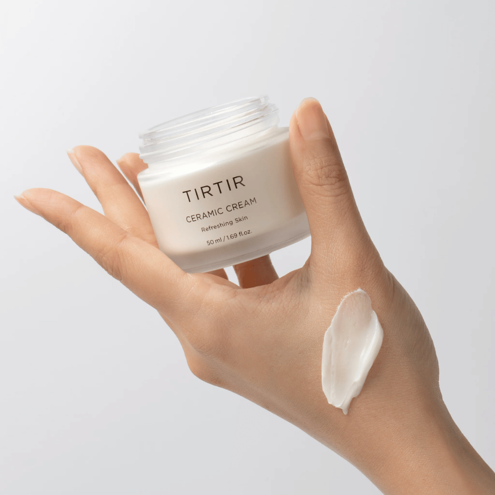 Roka drži kozarec s TIRTIR Ceramic Cream. Na hrbtni strani roke je nanesena količina kreme. Krema se zdi gosta in vlažilna. Embalaža navaja, da je vsebina za "Osvežitev kože" in količina je 50 ml / 1.69 fl oz.