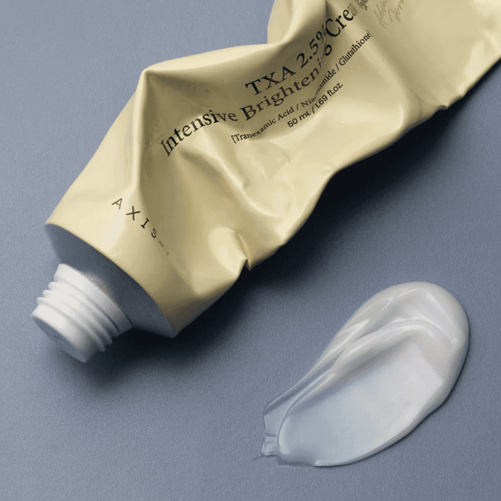 Produktna slika s tubo in kapljico kreme ob njej za prikaz mehke, kremaste teksture in vlažilne formule. Poudarek je na glow učinku in enakomernem nanosu.