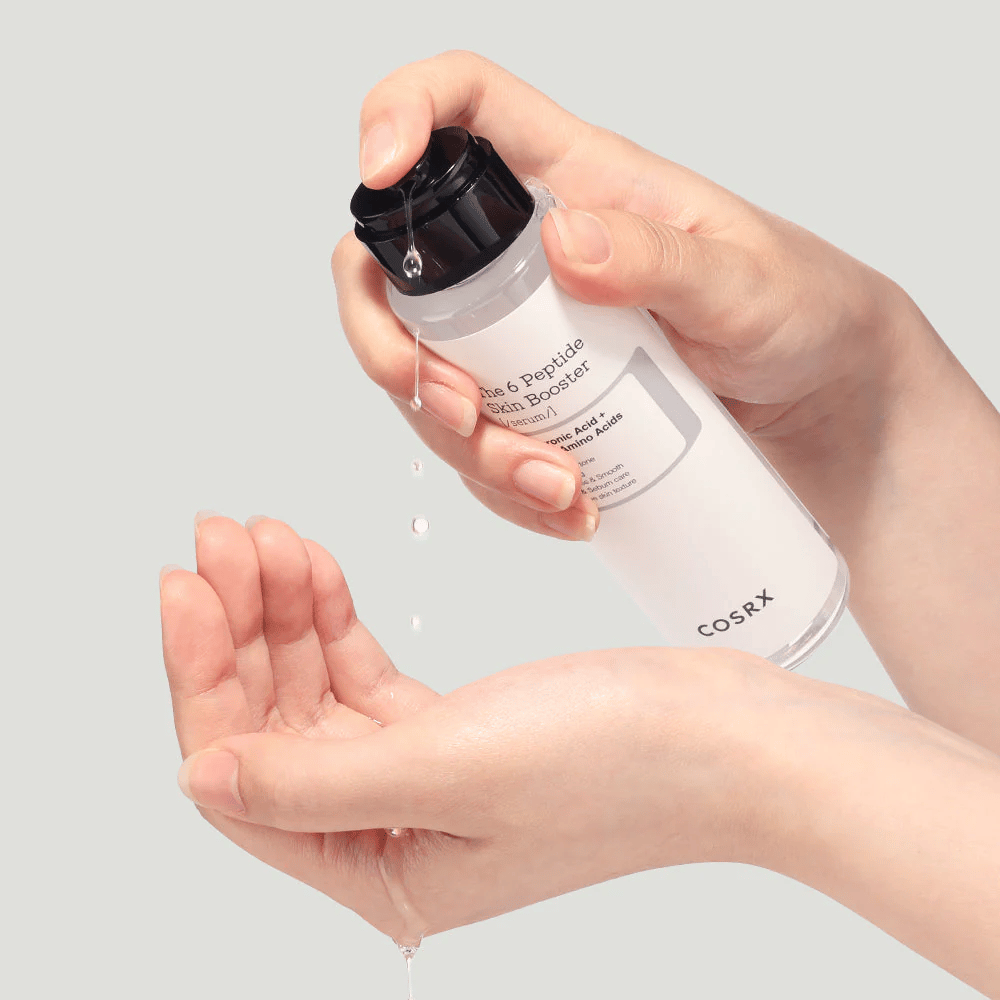 Roke, ki izlivajo negovalni izdelek iz prozorne stekleničke z napisom "The Peptide Skin Booster".