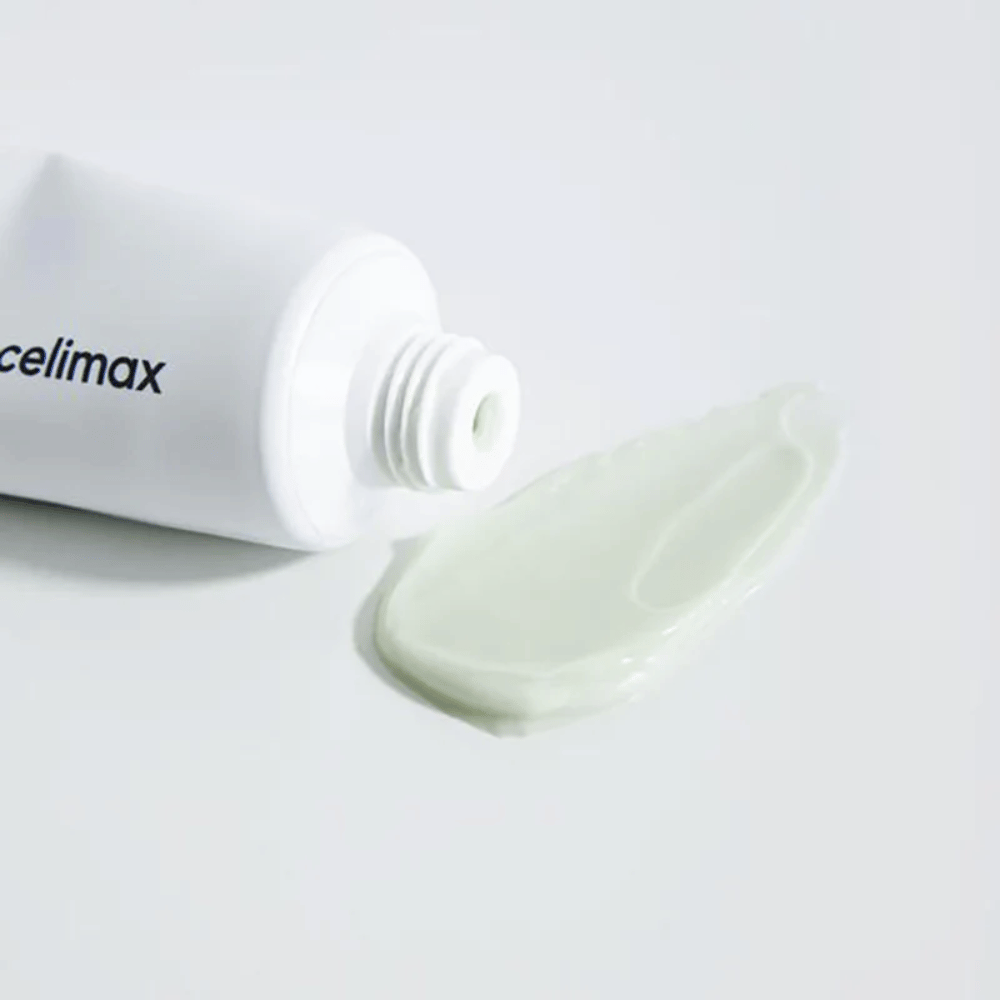 Celimax Noni Energy Repair Cream v beli tubi z majhno količino svetlo zelene kreme iztisnjene poleg tube na beli površini. Krema je namenjena negi in obnovi kože.