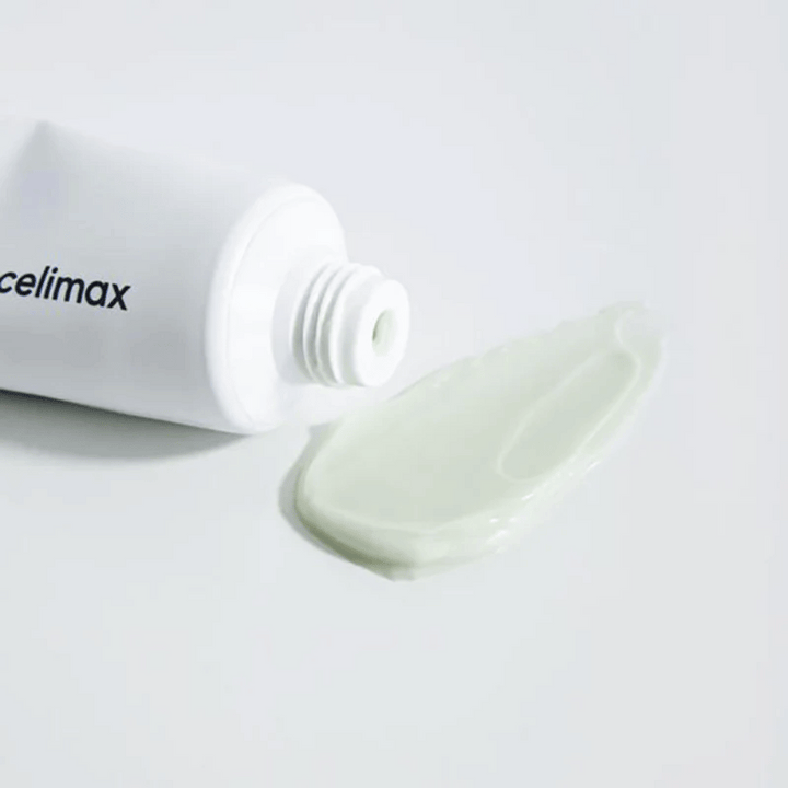 Celimax Noni Energy Repair Cream v beli tubi z majhno količino svetlo zelene kreme iztisnjene poleg tube na beli površini. Krema je namenjena negi in obnovi kože.