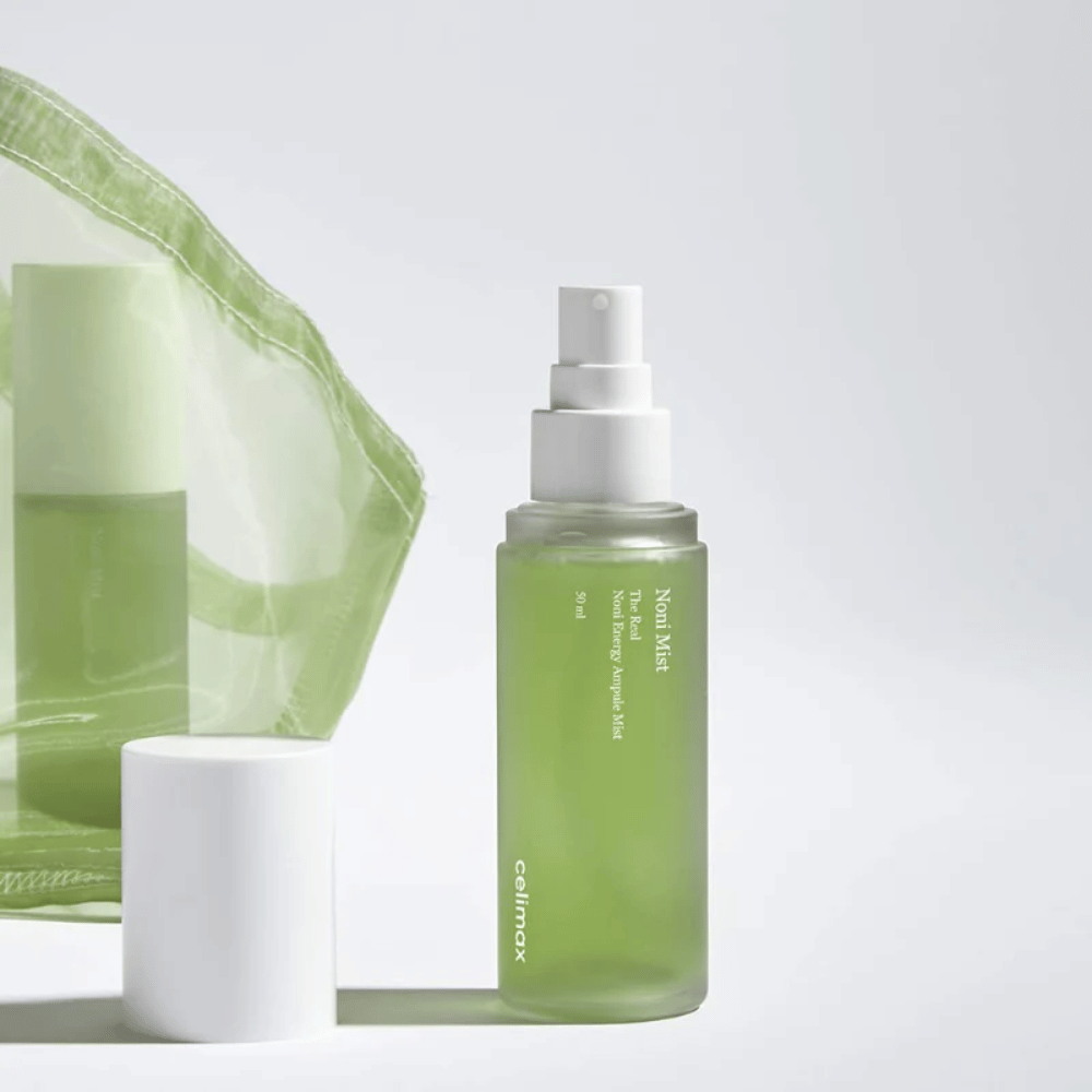 Steklenica Celimax Noni Mist, zelena razpršilna steklenica z belim črpalko, ki stoji poleg pokrovčka. Izdelek je pakiran v prozorno plastično vrečko in se trži kot Noni Energy Ampule Mist.