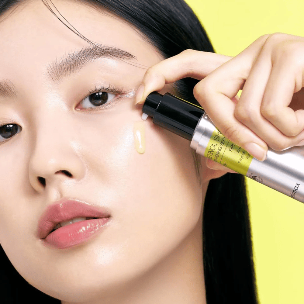 Model nanese The Vita-A Retinol Shot Tightening Serum od Tiam blizu predela okoli oči, s poudarkom na sijaju kože in rumeni konsistenci seruma.