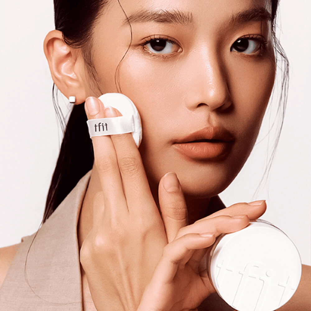 Ženska nanaša TFIT Translucent Set Finishing Powder #02 Skin Beige s puffom, drži belo škatlico pudra z logotipom TFIT.
