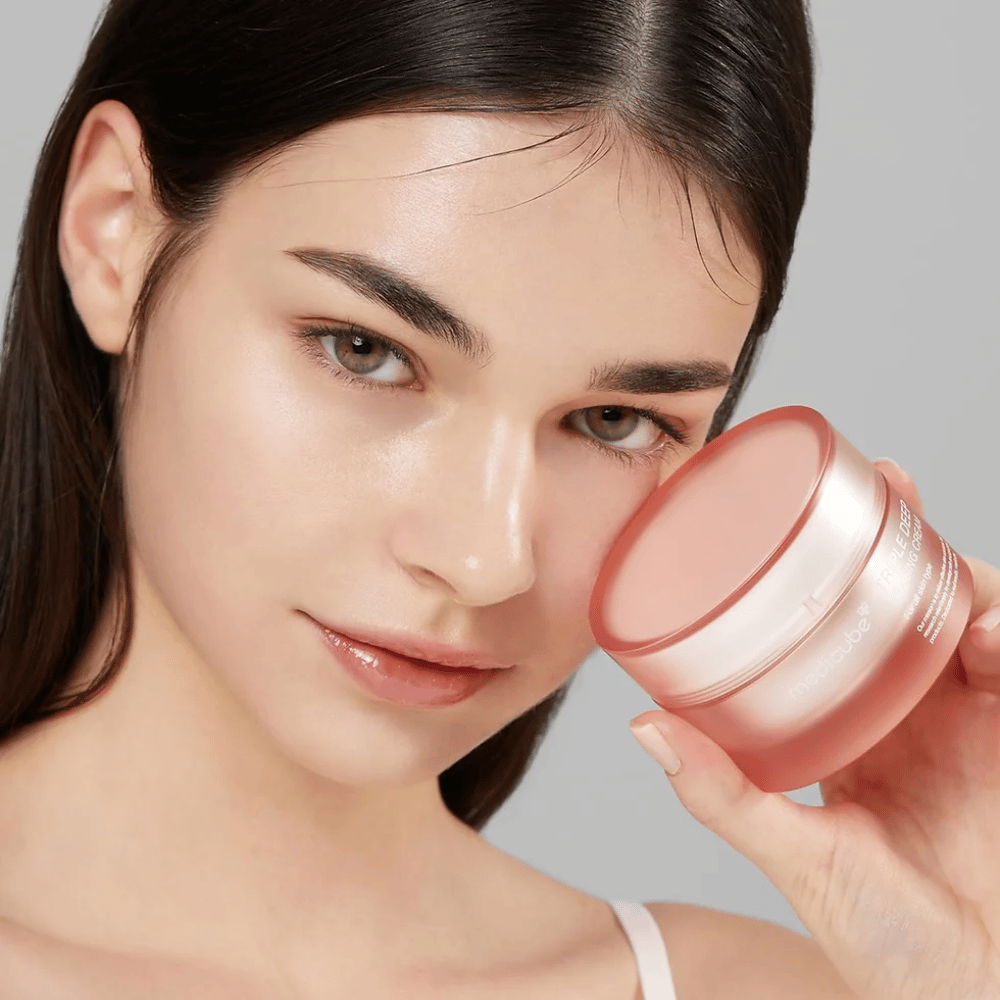 Slika prikazuje žensko, ki drži posodico s kremo Triple Collagen Cream. Krema je zasnovana za izboljšanje elastičnosti kože in vlaženja. Koža ženske je videti gladka in dobro negovana.




