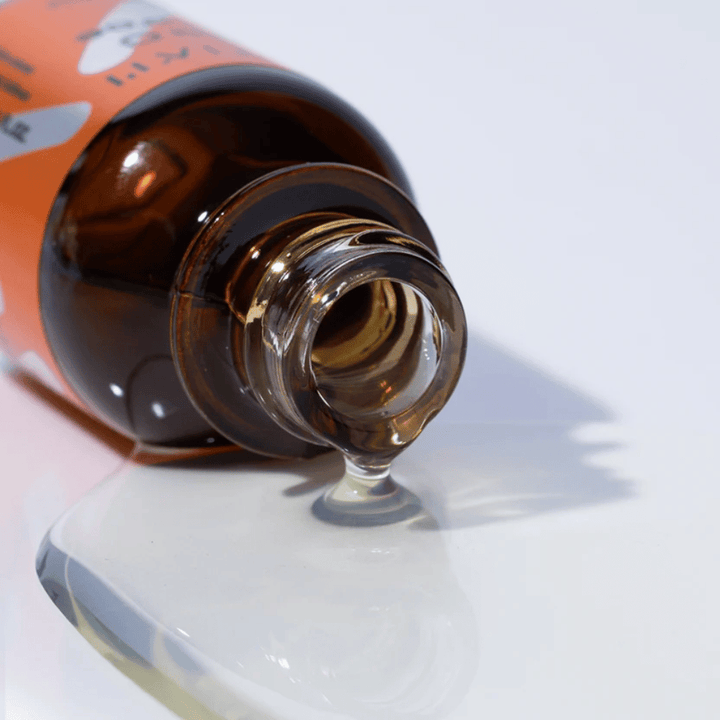 Povečava seruma TIA'M Vita C Source, ki teče iz rjave stekleničke. Jasna formula seruma poudarja njegovo koncentrirano vsebnost vitamina C za sijočo kožo.