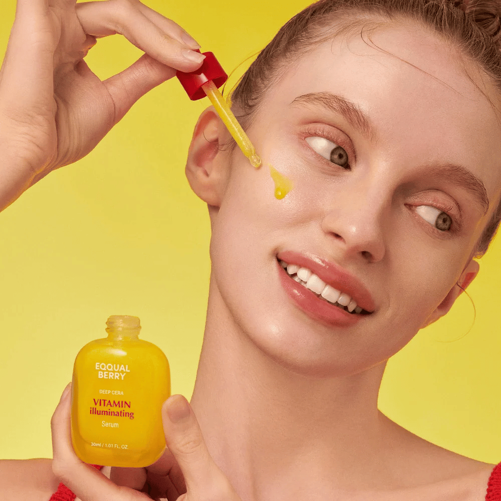 Nasmejana ženska nanaša Equal Berry Vitamin Illuminating Serum s pipeto. Sveža in sijoča koža na živahnem rumenem ozadju, ki se ujema z barvo seruma.