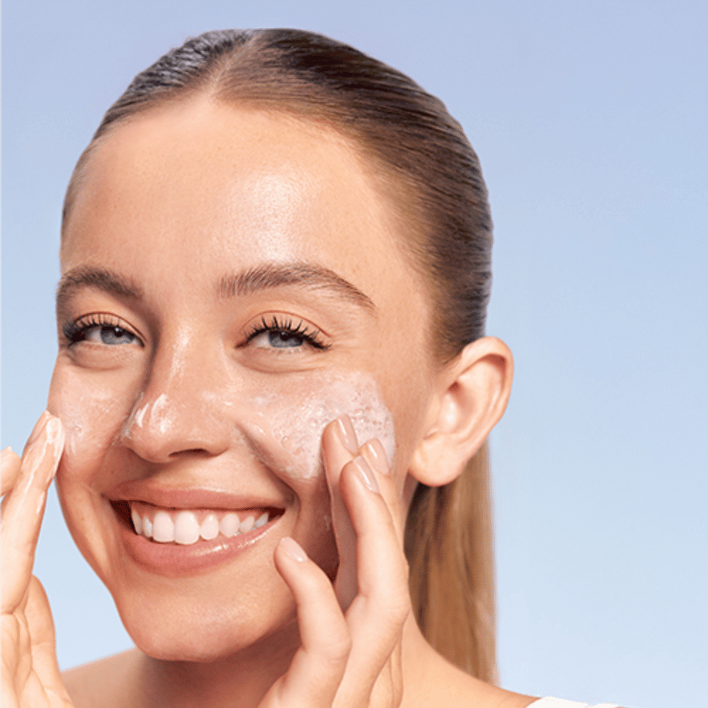 Nasmejana ženska nanaša LANEIGE Water Bank Gentle Gel Cleanser v penasti obliki na lica, na modri podlagi.