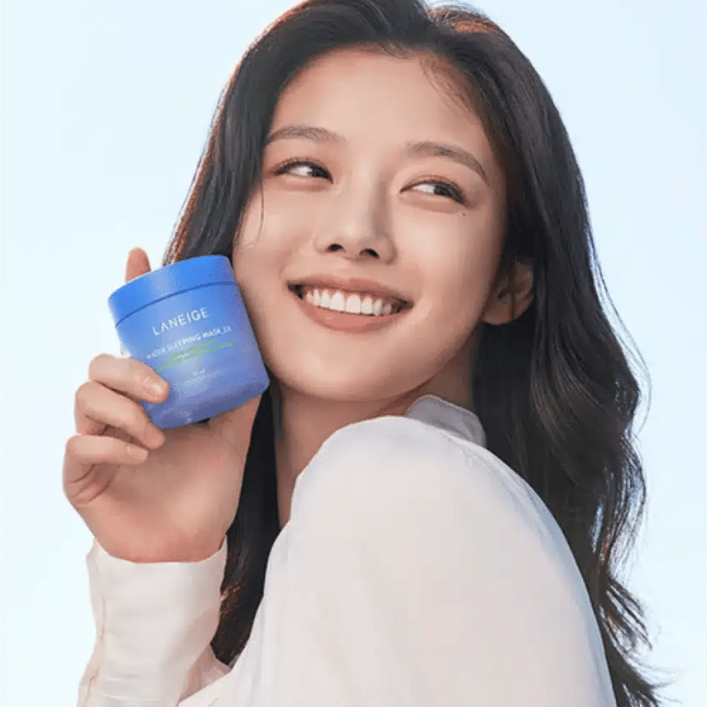 Nasmejana ženska drži modro posodo LANEIGE Water Sleeping Mask pred svetlo modro podlago.