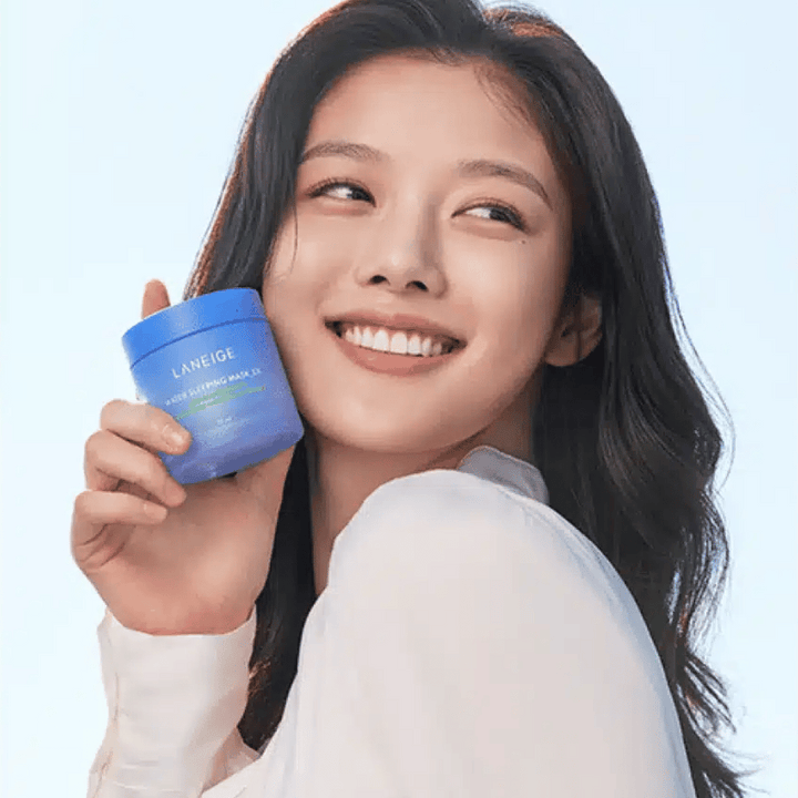 Nasmejana ženska drži modro posodo LANEIGE Water Sleeping Mask pred svetlo modro podlago.