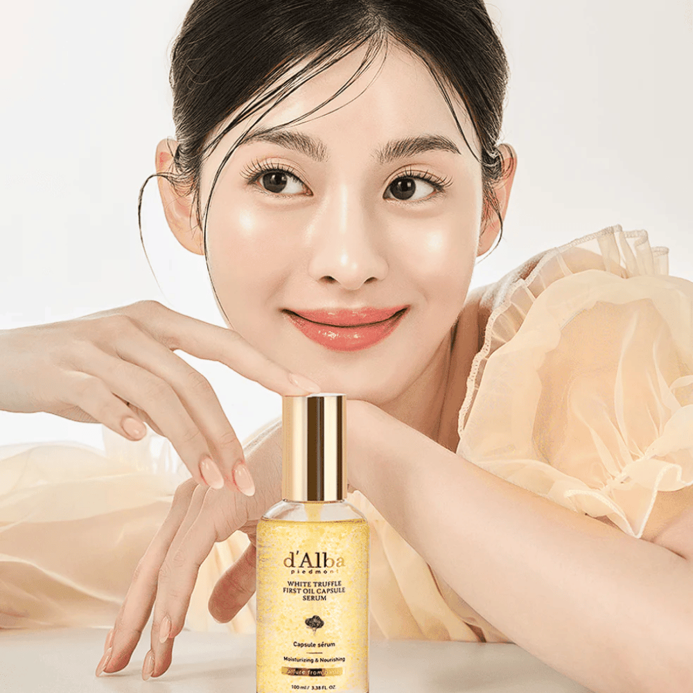 Model v svetli obleki se nežno smehlja poleg d'Alba White Truffle First Oil Capsule Serum.