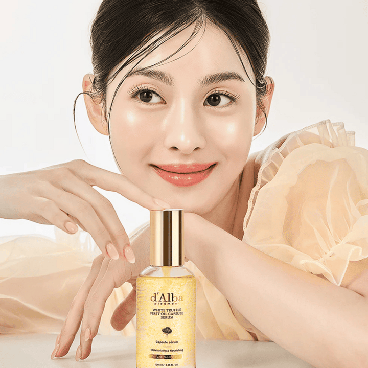 Model v svetli obleki se nežno smehlja poleg d'Alba White Truffle First Oil Capsule Serum.