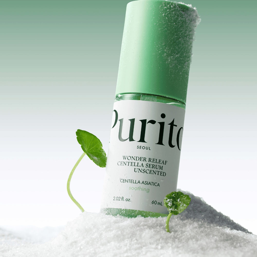 Steklenica Purito Centella Serum leži v snegu, vidni so zeleni listi, na mehki zeleni podlagi.