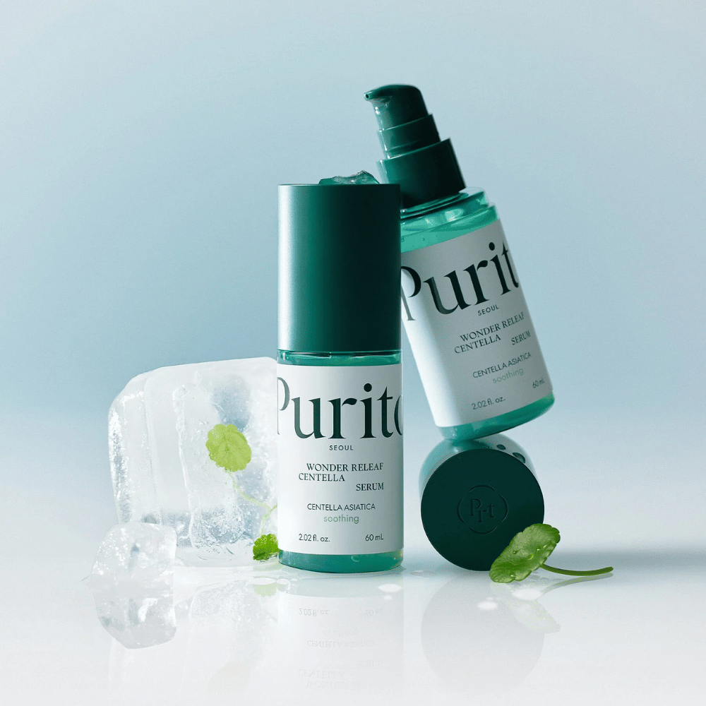 Dve steklenički Purito Wonder Releaf Centella Serum, ena stoječa in ena ležeča, obdani z ledenimi kockami s centelinimi listi znotraj ter enim prosto ležečim listom na svetlo modri površini.