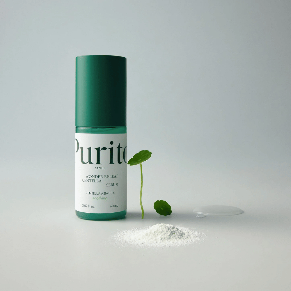 Zelena steklenička Purito Wonder Releaf Centella Serum 60 ml stoji na beli podlagi, obdana s centelinimi listi, prozorno kapljico seruma in majhnim belim prahom.