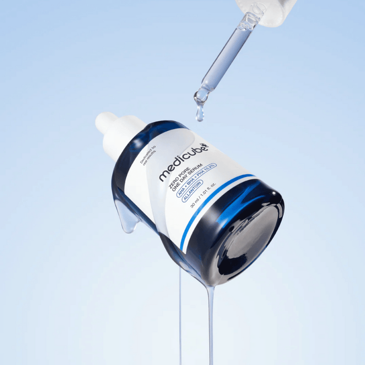 Steklenica Medicube Zero Pore One Day Serum s pipeto in kapljajočimi kapljicami seruma na svetlo modri podlagi.
