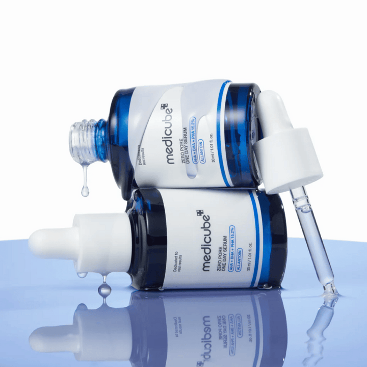 Dve modri steklenici Medicube Zero Pore One Day Serum, ki ležita ena ob drugi, s pipetami in kapljicami seruma na odsevni modri površini.