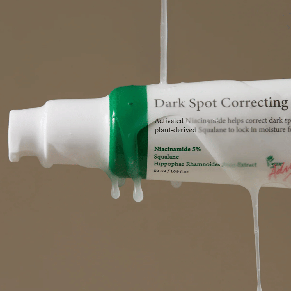 Bližnji posnetek stekleničke s pumpico Axis-Y Dark Spot Correcting Glow Serum z belo embalažo in zelenim pokrovčkom, prekrita s tekočo prozorno tekočino.