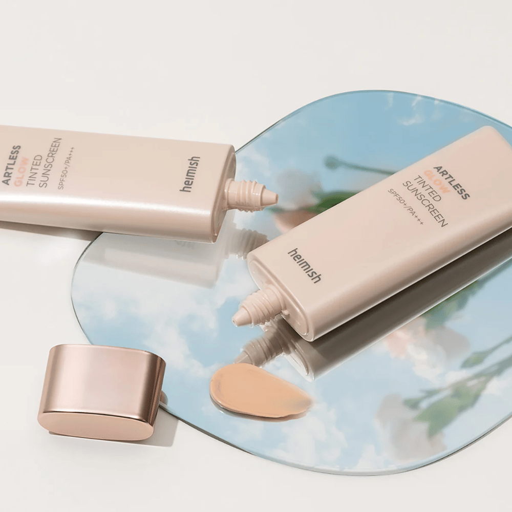 Steklenica heimish Artless Glow Tinted Sunscreen SPF50+ PA+++ 40ml in steklenica korektorja na ogledalu, ki prikazuje različne tone kože.