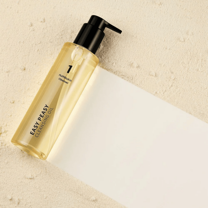 Numbuzin No.1 Easy Peasy Cleansing Oil leži na peščeni površini s senco.