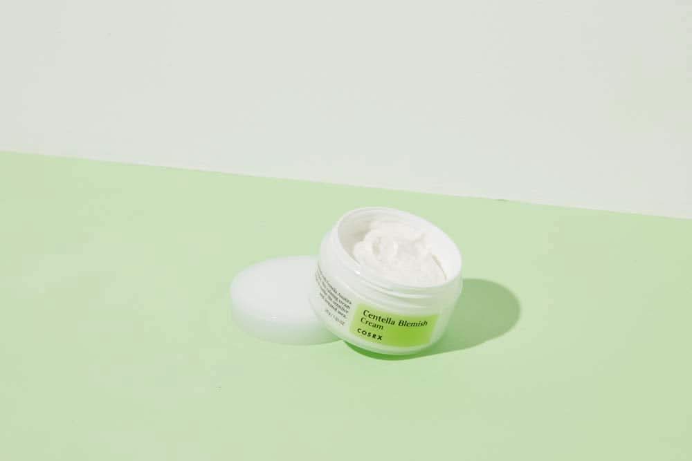 Kozarec COSRX Centella Blemish Cream 30ml, ki stoji na zeleni površini.
