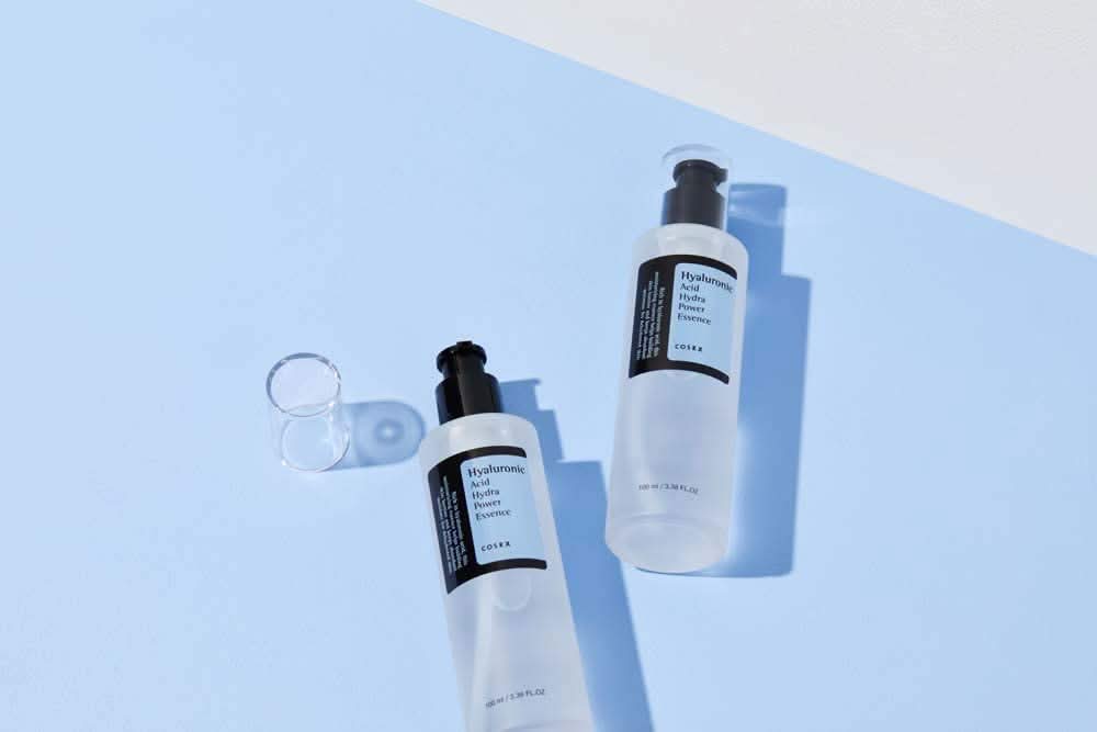 COSRX-ov Hyaluronic Acid Hydra Power Essence 100ml zagotavlja vlažilne prednosti na modri površini.