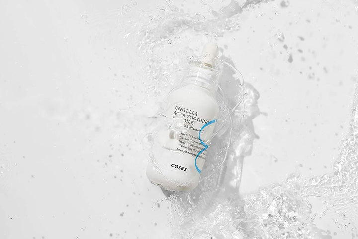 Steklenica COSRX Centella Aqua Soothing Ampoule 40ml, ki prši na belo površino, zmanjšuje rdečico in zagotavlja pomirjujočo hidratacijo.