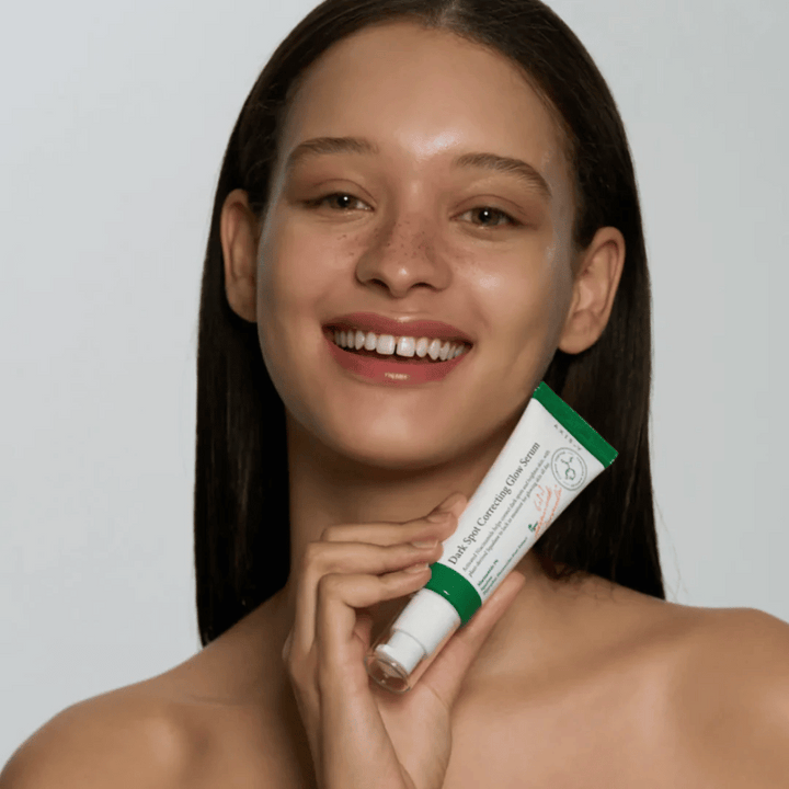 Mlada ženska drži tubo AXIS - Y Dark Spot Correcting Glow Serum 50ml.