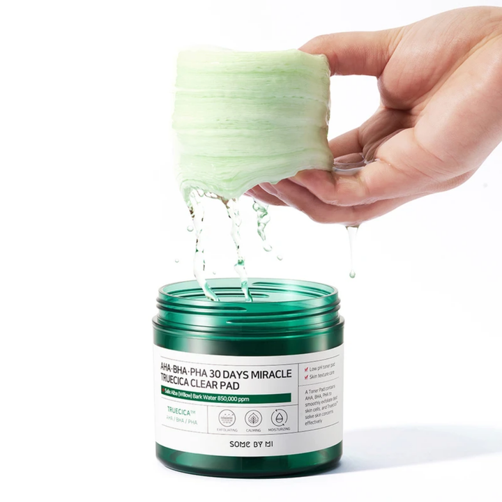 Roka drži zeleno tekočino v posodi za SOME BY MI's AHA, BHA, PHA 30 Days Miracle Truecica Clear Pad 70 kos zdravljenje izbruhov aken.