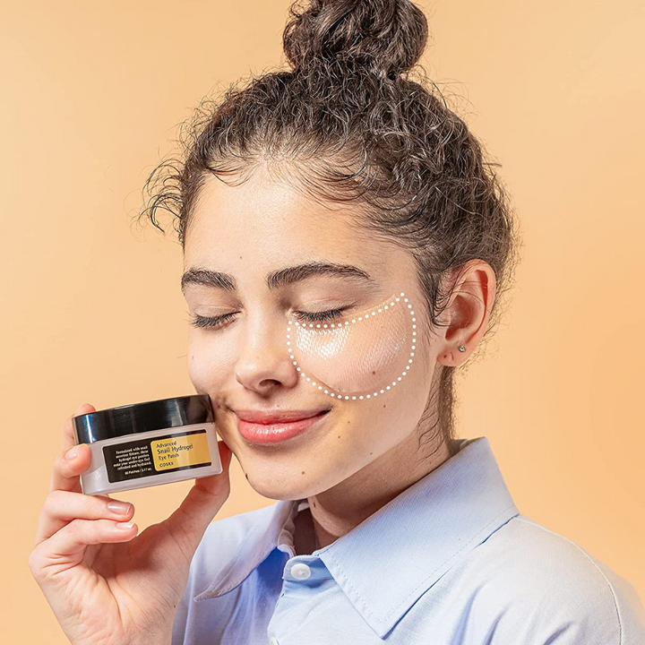 Ženska, ki drži posodo COSRX Advanced Snail Hydrogel Eye Patch 60 kosmičev kreme za obraz.