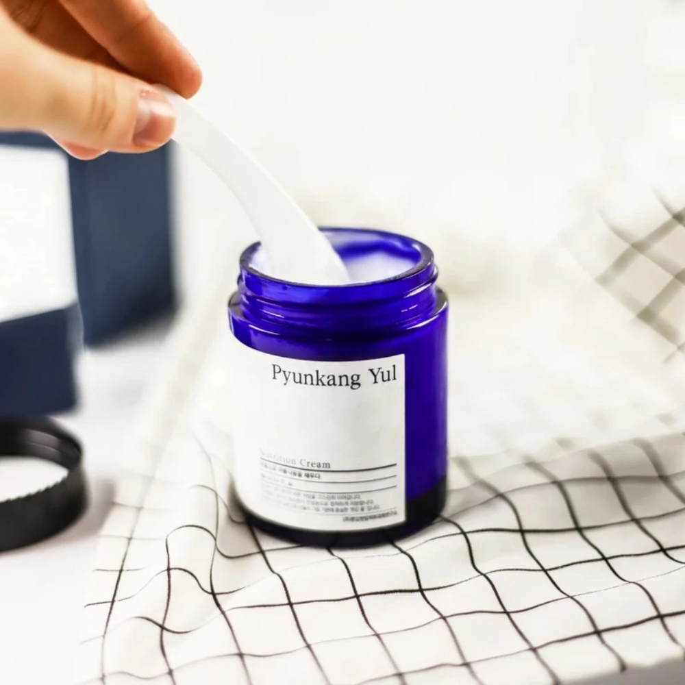 Oseba uporablja kozarec Pyunkang Yul Nutrition Cream 100ml na mizi.