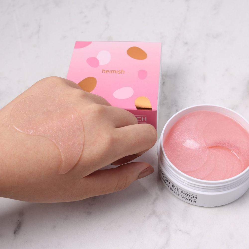 Roka, ki drži roza Bulgarian Rose Hydrogel Eye Patch 60st iz heimish in nanese očesno masko.