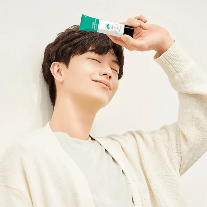 Mladenič ščiti svojo občutljivo kožo pred UV-žarki tako, da drži tubo SOME BY MI Truecica Aqua Calming Sun Cream 50ml na glavi.