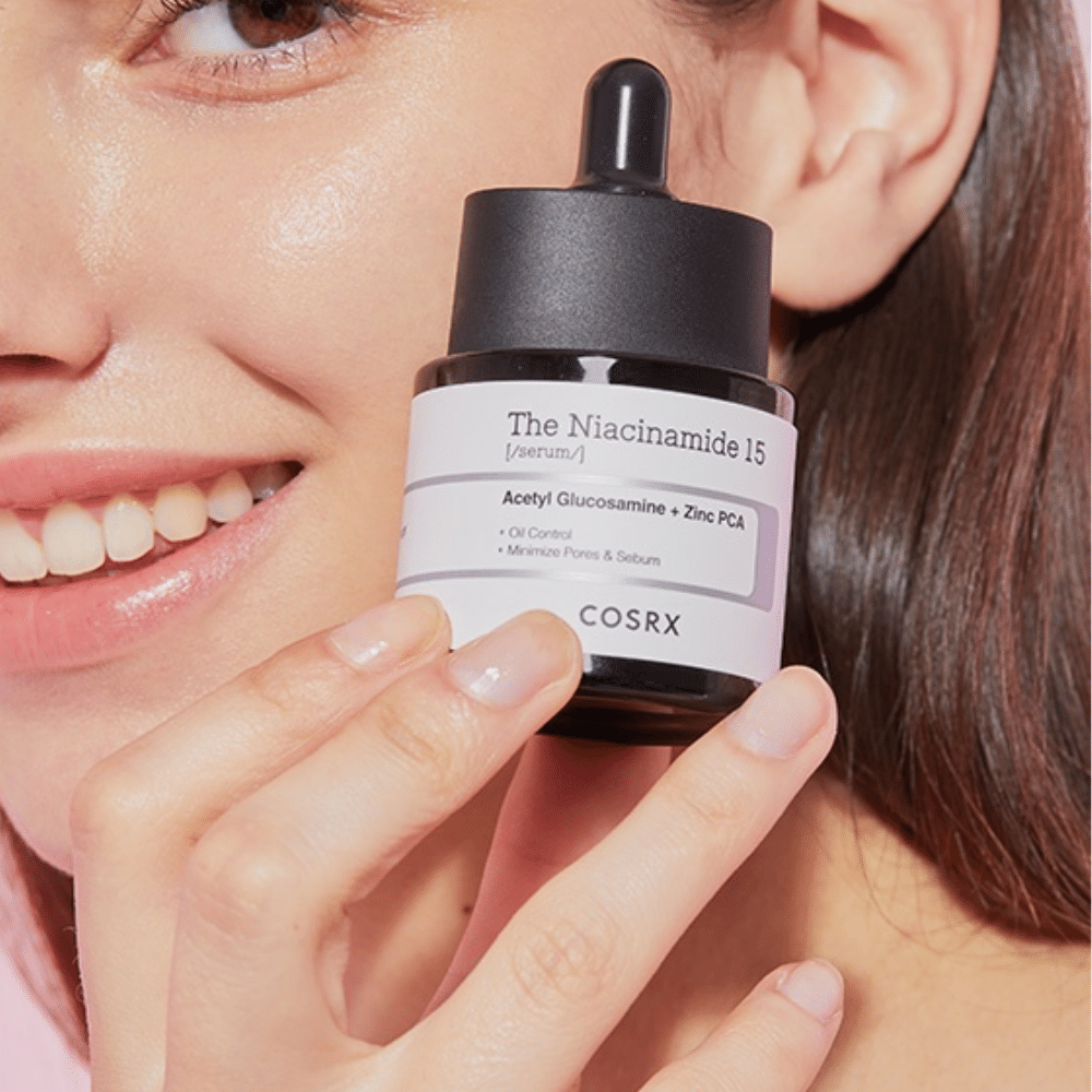 Ženska drži stekleničko COSRX Niacinamide 15 Serum 20ml za niacinamid in proizvodnjo sebuma.