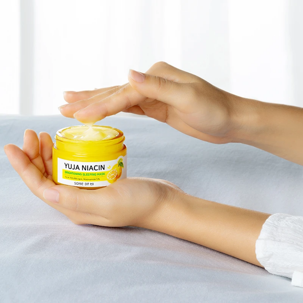 Ženska roka, ki drži posodo SOME BY MI Yuja Niacin Brightening Sleeping Mask 60g za neenakomerno polt.