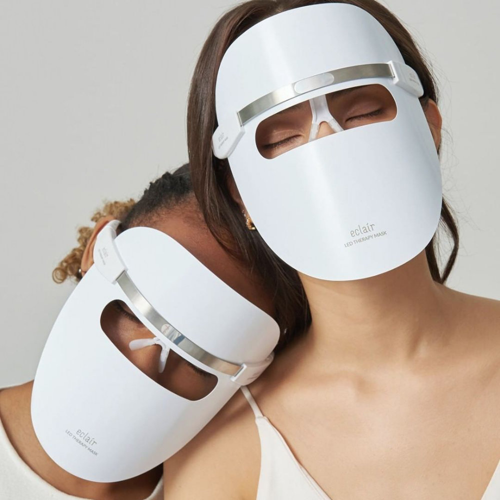 Dve ženski, ki nosita bele maske, demonstrirata ECLAIR LED Therapy Mask za izboljšanje tona kože.