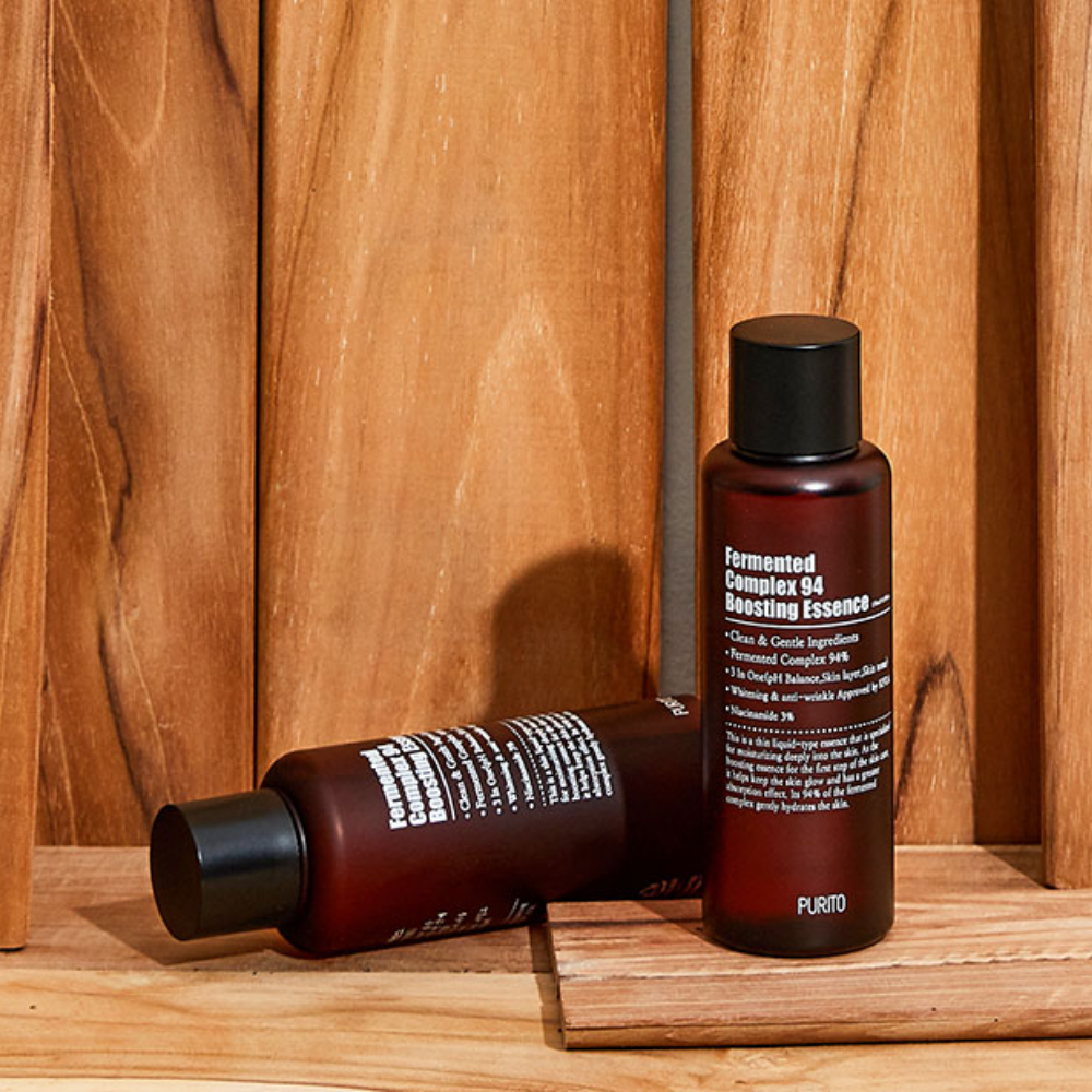 Dve steklenici PURITO Fermented Complex 94 Boosting Essence 150ml za zmanjšanje drobnih linij in gub, ki stojita na leseni mizi.