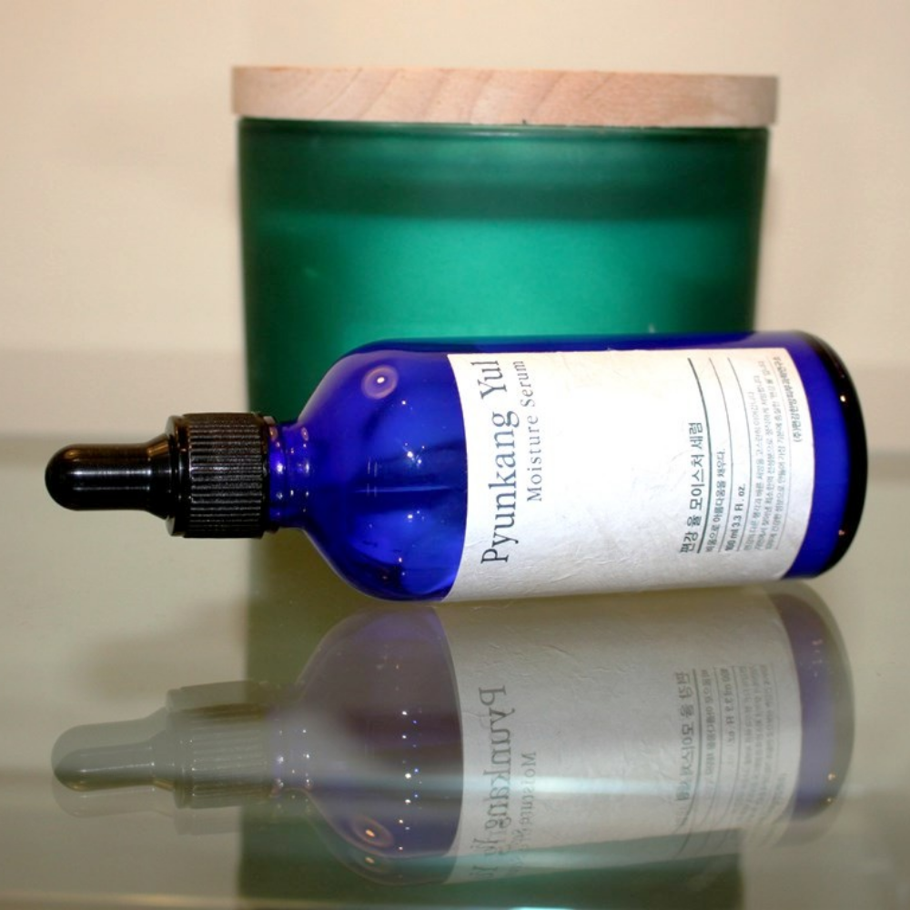Steklenica Pyunkang Yul Moisture Serum 100 ml uravnava nivo vlage na mizi poleg sveče.