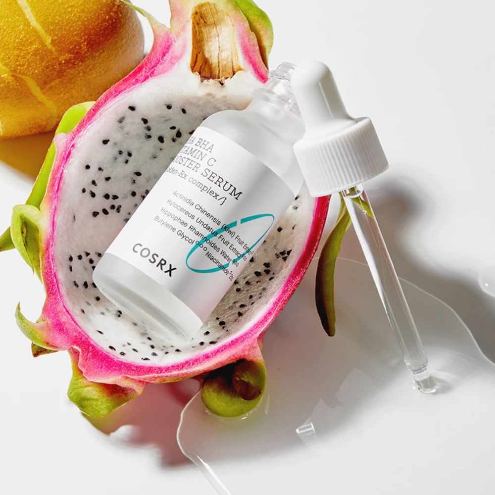 Korejski izdelek za nego kože, COSRX Refresh AHA BHA Vitamin C Booster Serum 30 ml, s stekleničko seruma iz zmajevega sadja poleg rezine sadja.