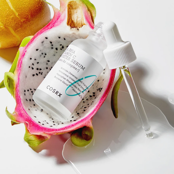 Korejski izdelek za nego kože, COSRX Refresh AHA BHA Vitamin C Booster Serum 30 ml, s stekleničko seruma iz zmajevega sadja poleg rezine sadja.