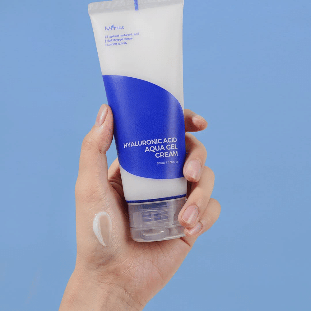 Roka, ki drži tubo Isntree Hyaluronic Acid Aqua Gel Cream 100ml na modrem ozadju.