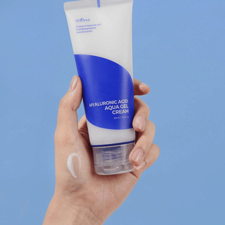 Roka, ki drži tubo Isntree Hyaluronic Acid Aqua Gel Cream 100ml na modrem ozadju.