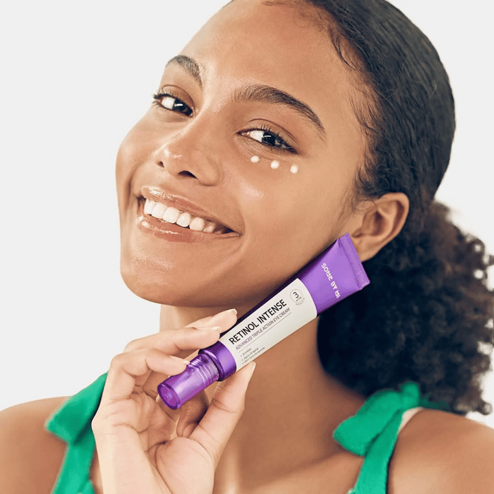 Ženska, ki se smeji, medtem ko drži tubo SOME BY MI Retinol Intense Advanced Triple Action Eye Cream 30ml.